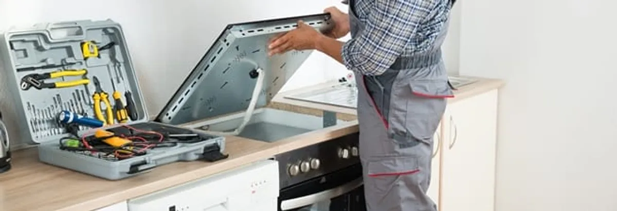 Cooktop repair technician lifting a built-in stovetop for service in Louisville, KY