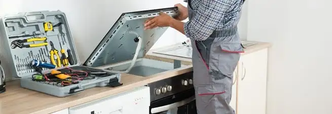 Cooktop repair technician lifting a built-in stovetop for service in Louisville, KY