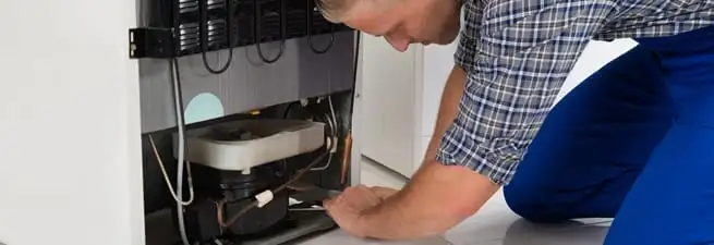 Refrigerator repair technician servicing the compressor and condenser area in Louisville, KY