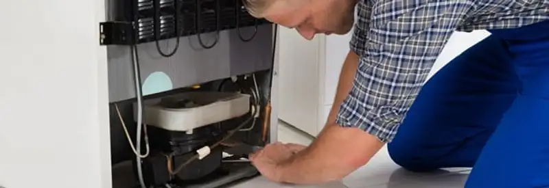 Refrigerator repair technician servicing the compressor and condenser area in Louisville, KY