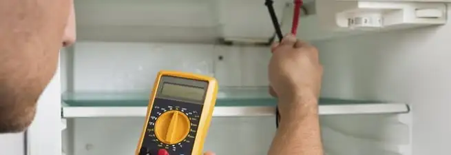 Refrigerator repair technician testing electrical components with a multimeter in Louisville, KY