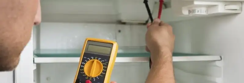 Refrigerator repair technician testing electrical components with a multimeter in Louisville, KY